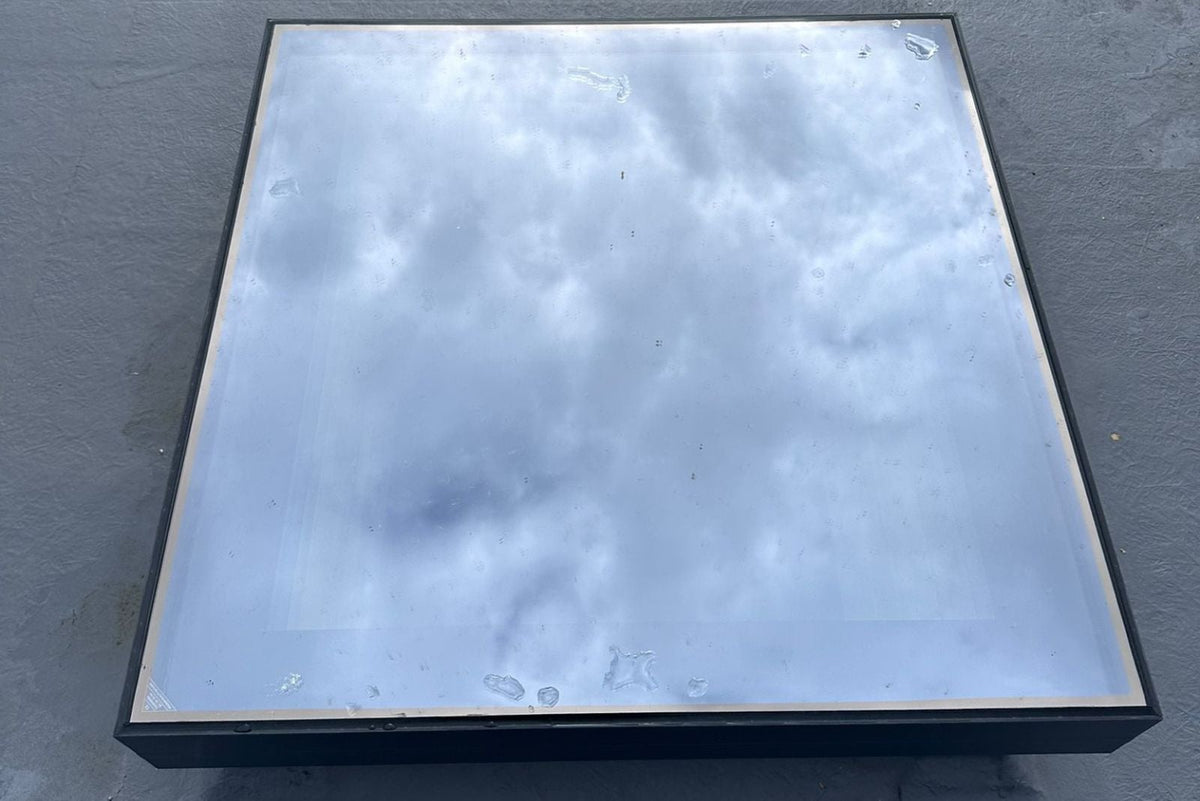 Gerahmtes festverglastes Dachfenster von oben – schmaler Aluminiumrahmen, die Glasfläche spiegelt den Himmel