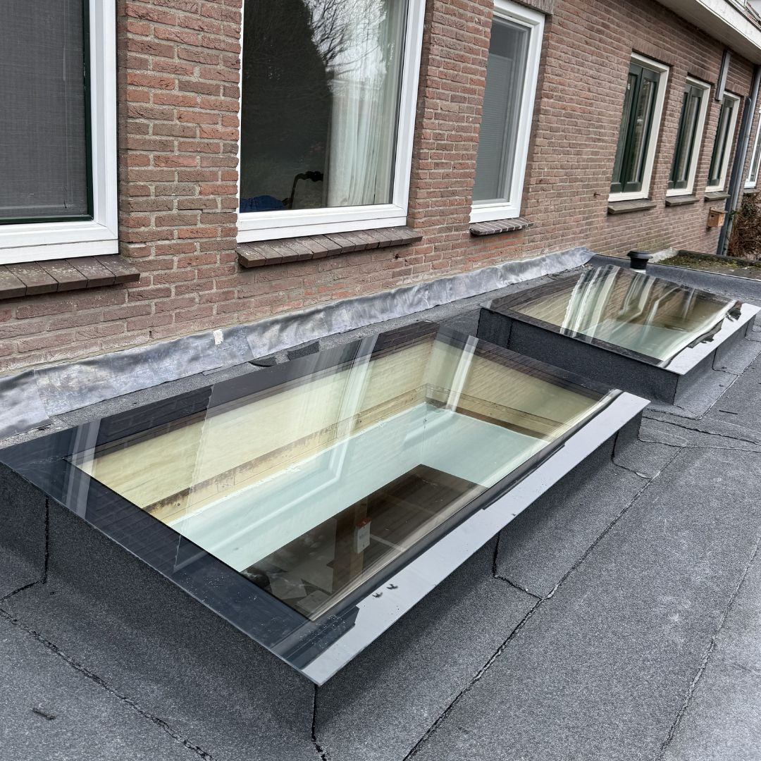 Zwei lange rahmenlose Dachfenster nach Maß auf dem Flachdach eines Anbaus vor einer Ziegelfassade